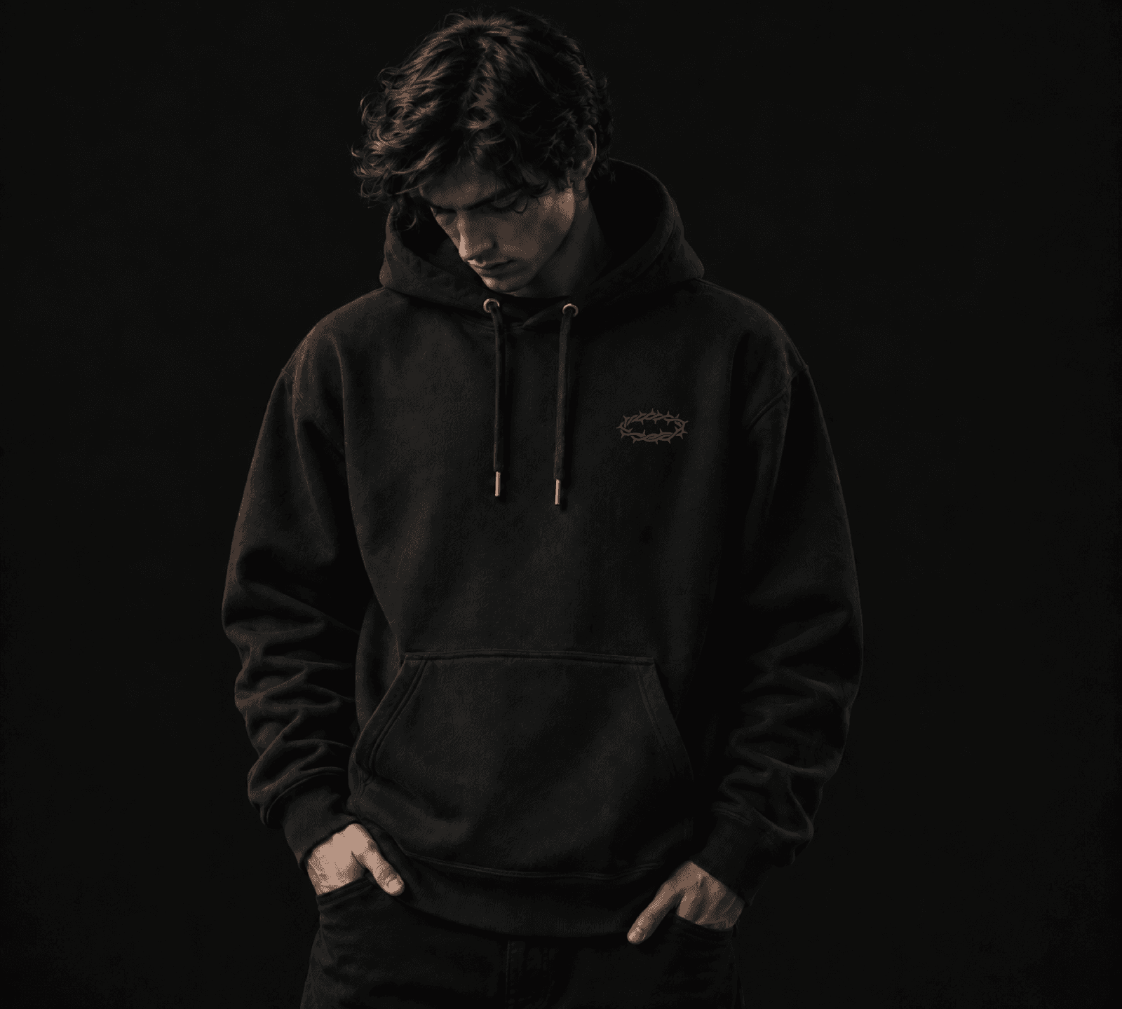 Model looking down while wearing the black SUESTAUROMAI hoodie with the crown at the left chest.